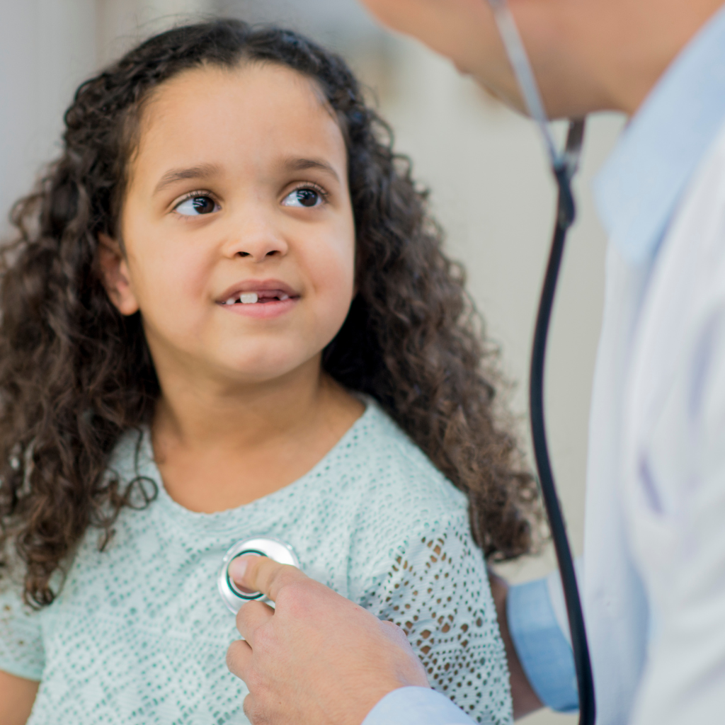 Young girl in doctors office with doctor using stethescope on her heart during a pediatric care checkup.
